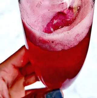 a hand holding a champagne flute with raspberry sorbet mimosa