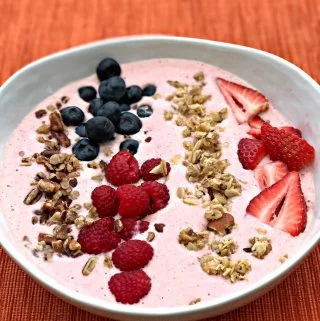 almond butter berry power protein smoothie topped with granola, blueberries, raspberries, and sliced strawberries in a white bowl