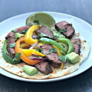 grilled steak fajitas on a tortilla on a white plate