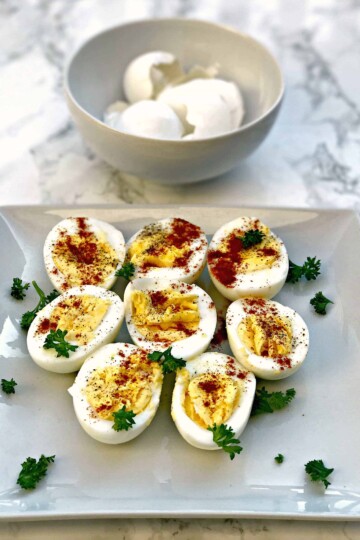 sliced hard boiled eggs on a square plate and a bowl of peeled egg shells