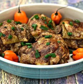 Jamaican jerk chicken thighs on a serving platter garnished with green onions and habanero peppers