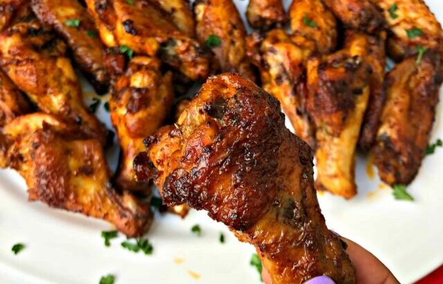 person holding air fryer buffalo chicken wing over a white plate of wings