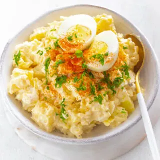 Instant Pot potato salad in a white bowl with boiled eggs and sprinkled with paprika