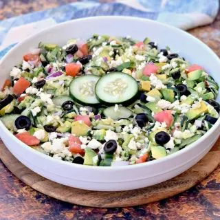 keto zucchini noodles pasta salad in a white bowl with tomatoes, olives, cucumbers, feta cheese, and red onions