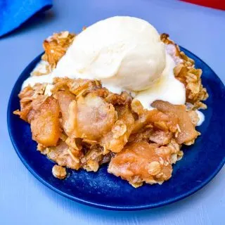 healthy apple crisp on a blue plate with vanilla ice cream