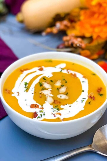 Panera copycat autumn squash soup in a white bowl with seeds and bacon