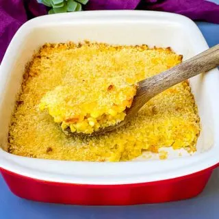 a wooden spoonful of scalloped corn in a baking dish