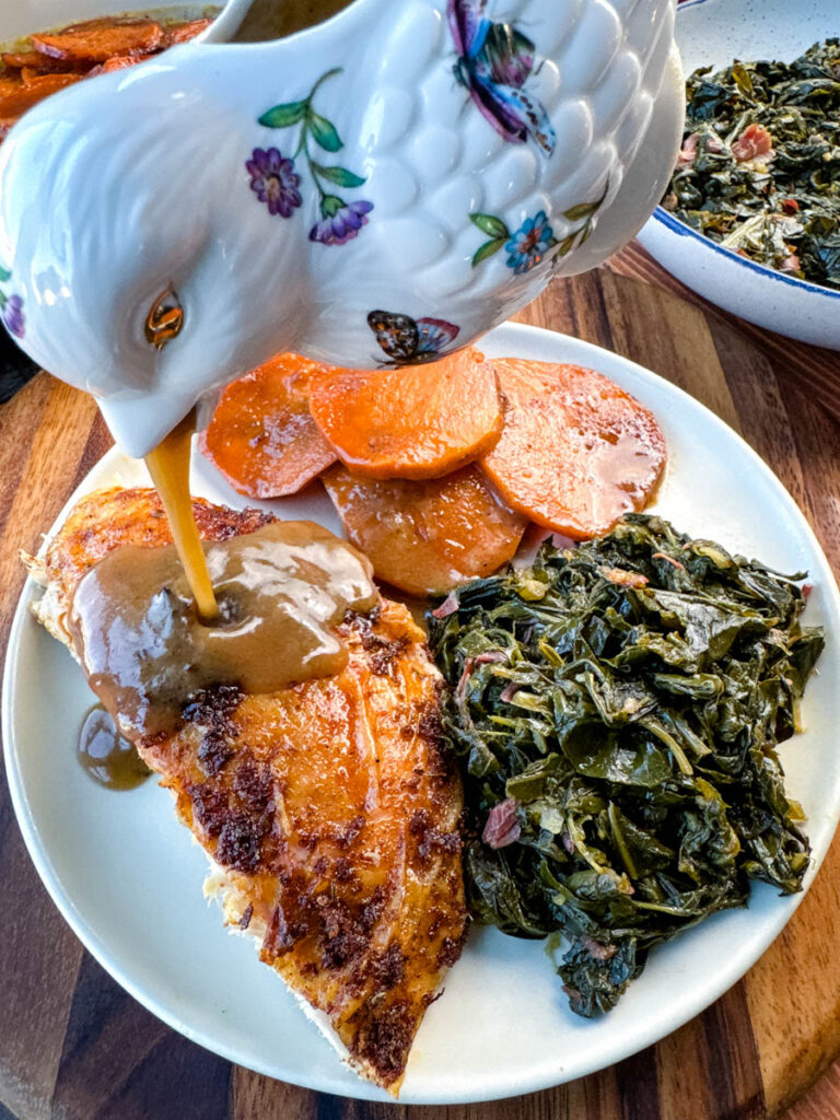 gravy drizzled over Cajun turkey on a plate with gravy, collard greens, and candied sweet potatoes