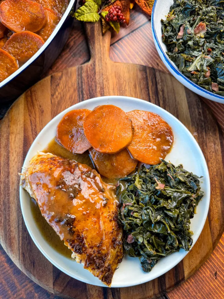 Cajun turkey on a plate with gravy, collard greens, and candied sweet potatoes