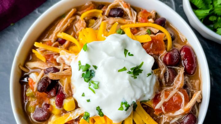 buffalo chicken chili in a white bowl with shredded cheese and sour cream