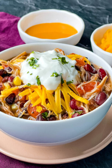 buffalo chicken chili in a white bowl with shredded cheese and sour cream