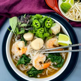 seafood shrimp pho in a white bowl drizzled with Sriracha