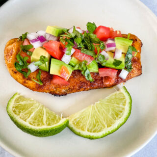 cooked chicken and avocado salsa on a plate with limes