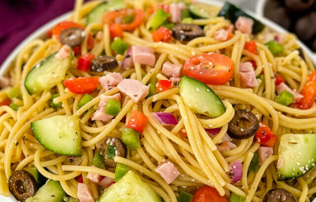 spaghetti salad in a white bowl with tomatoes and olivess