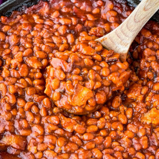 a wooden spoonful of Southern baked beans in a cast iron skillet