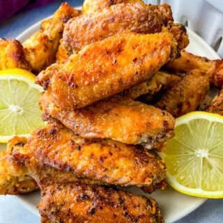 lemon pepper chicken wings on a white plate with fresh lemons