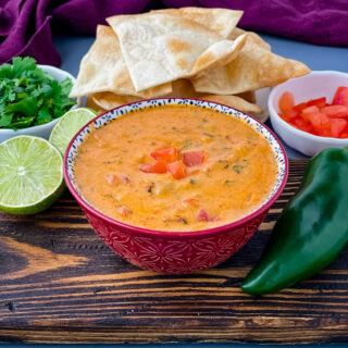 queso cheese dip in a red bowl with a plate of chips