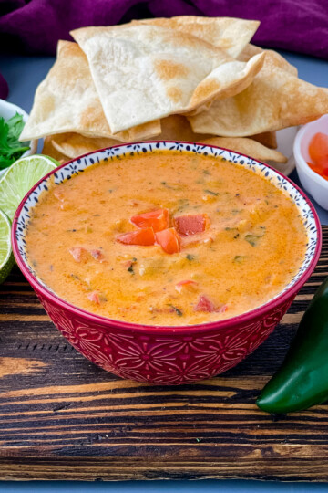 queso cheese dip in a red bowl with a plate of chips