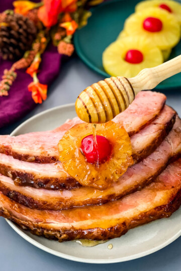 ham sliced on a plate with pineapples, cherries, and drizzled in honey