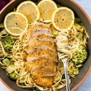 lemon chicken pasta in a pan with fresh lemons, spinach, and broccoli