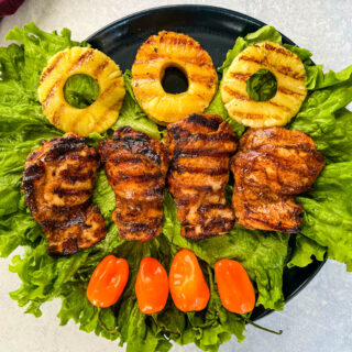 Jamaican jerk chicken thighs on a plate with peppers and grilled pineapples