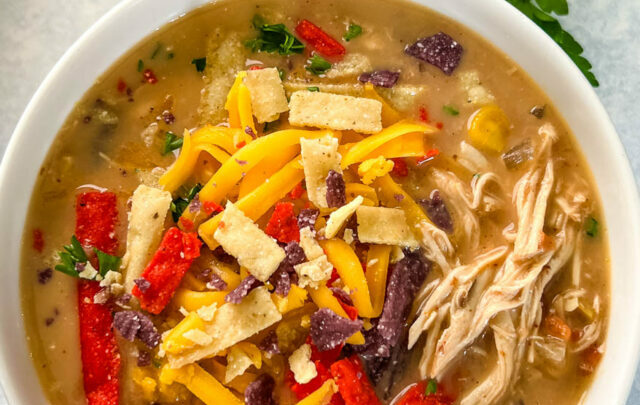 slow cooker chicken taco soup in a white bowl with tortilla strips and cheese