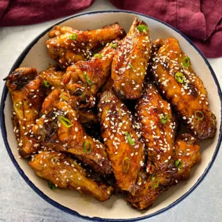 teriyaki chicken wings in a white and blue bowl with sesame seeds