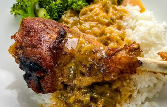 baked turkey leg on a plate with rice, gravy, and broccoli