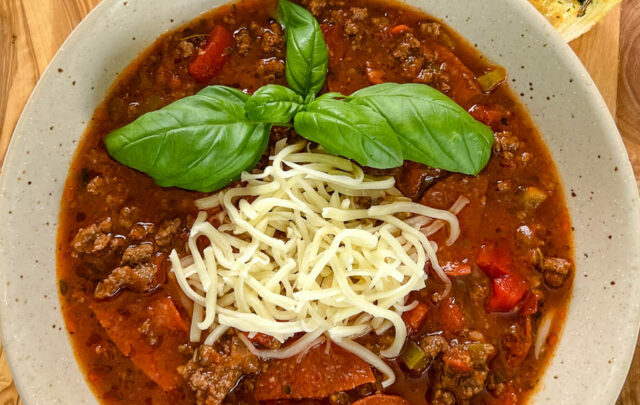 pizza soup with ground beef, pepperoni, mozzarella, and basil in a bowl