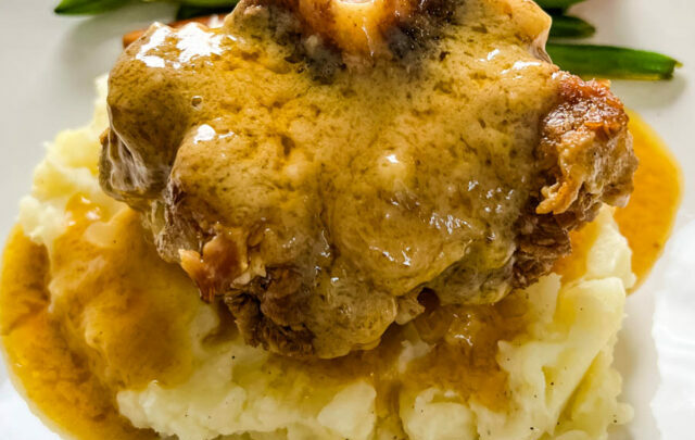 slow cooker crockpot oxtails with mashed potatoes, gravy, green beans, and carrots on a plate