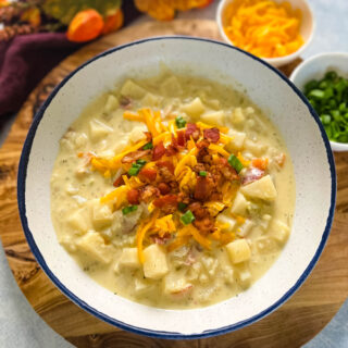 slow cooker loaded potato soup in a white bowl with bacon and cheese