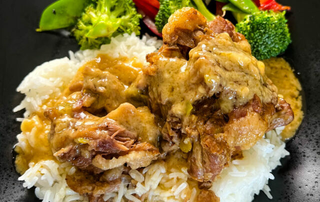 oxtail on a plate with white rice, gravy, and vegetables