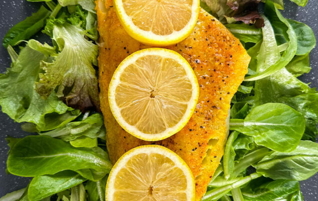 smoked cod fillet with lemons on a pan with greens