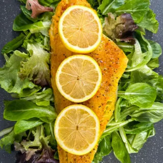 smoked cod fillet with lemons on a pan with greens