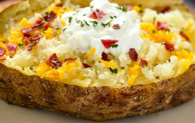 smoked baked potatoes on a plate loaded with sour cream, cheese, and bacon