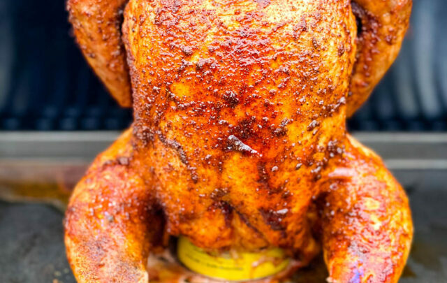 cooked, smoked seasoned whole chicken on a beer can in a Traeger smoker pellet grill