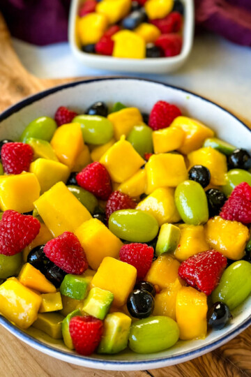 mango fruit salad with raspberries, blueberries, grapes, and avocado in a white bowl