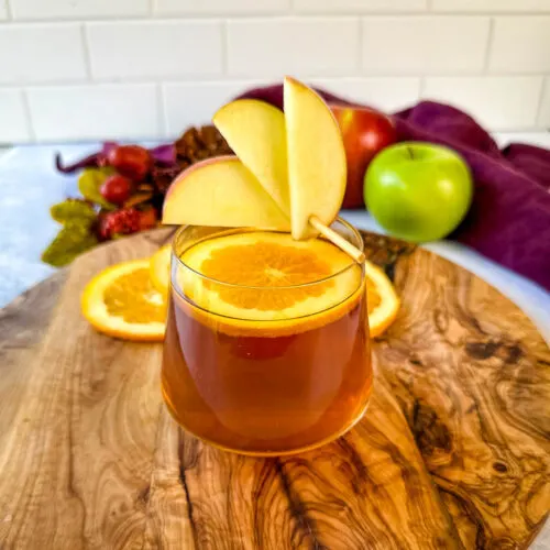 apple cider bourbon cocktail with orange and apple slices in a cup