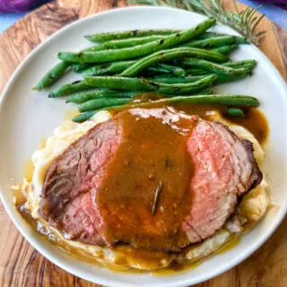 sliced eye of round roast beef on a plate with mashed potatoes, green beans, and au jus gravy