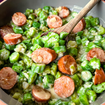 smothered okra with sausage and gravy in a skillet with a wooden spoon