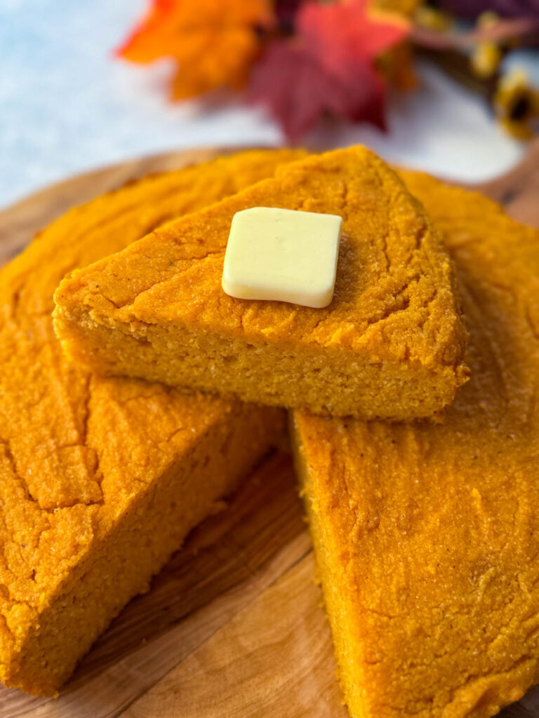a slice of sweet potato cornbread with butter on top of a pan of sweet potato cornbread