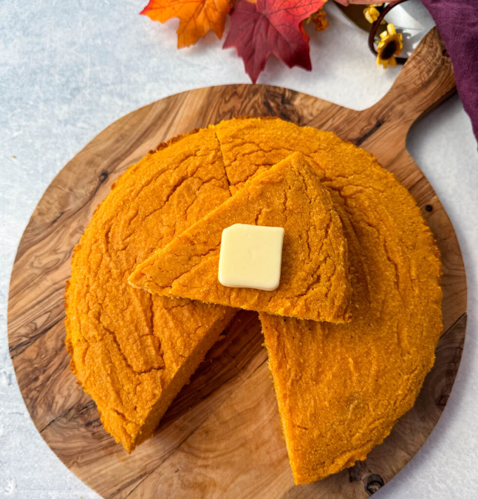 a slice of sweet potato cornbread with butter on top of a pan of sweet potato cornbread
