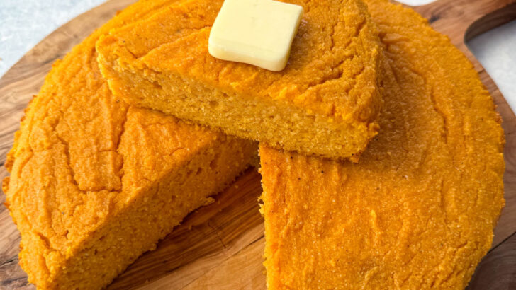 a slice of sweet potato cornbread with butter on top of a pan of sweet potato cornbread