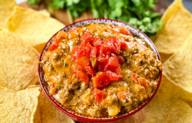 Rotel cheese dip with ground beef in a bowl with a plate of chips and cilantro