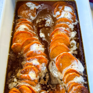 candied sweet potatoes with marshmallows in a baking dish drizzled with glaze in a wooden spoon