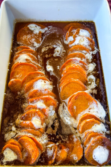 candied sweet potatoes with marshmallows in a baking dish drizzled with glaze in a wooden spoon