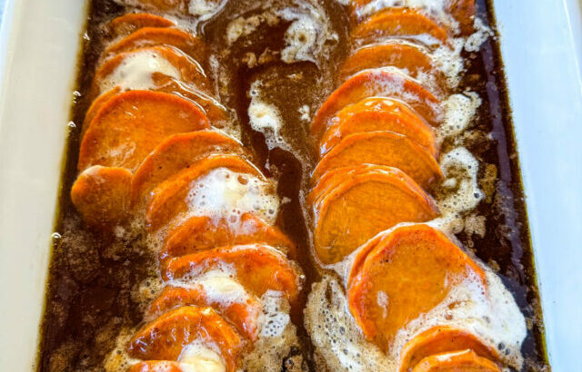 candied sweet potatoes with marshmallows in a baking dish drizzled with glaze in a wooden spoon