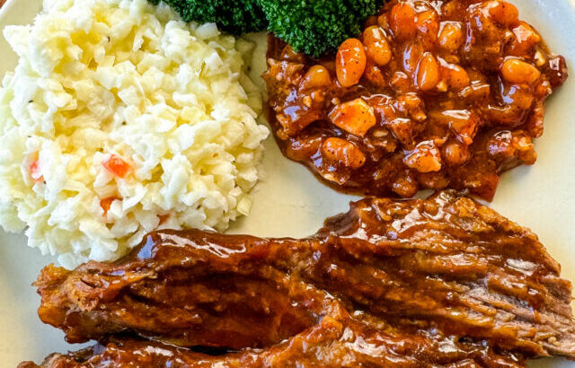 slow cooker Crockpot beef brisket with BBQ sauce on a plate with beans, broccoli, and coleslaw