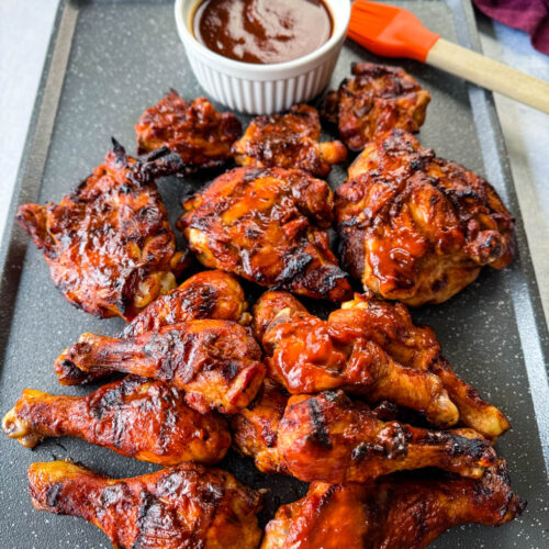 grilled bbq chicken thighs and drumsticks on a sheet pan with bbq sauce