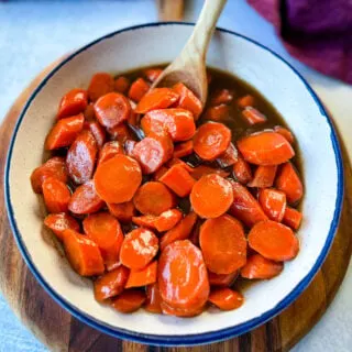 candied carrots with brown sugar cinnamon glaze in a white bowl with a wooden spoon